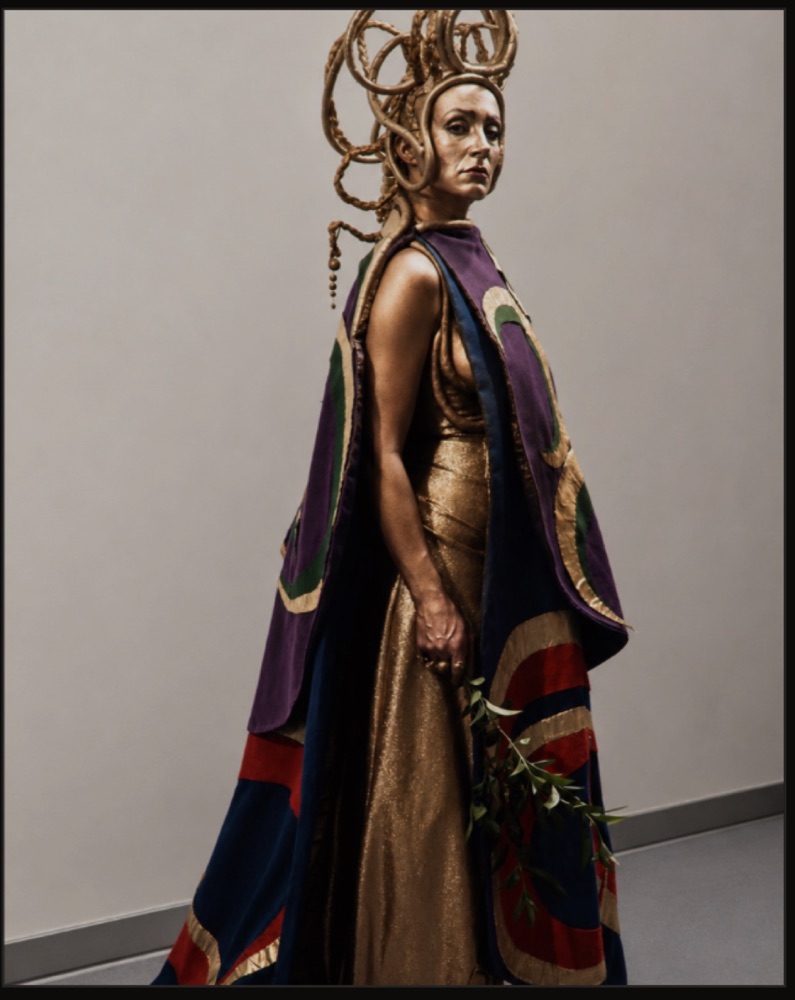 Electra production costume in gold with a purple cape and sculptural headdress, costumes by Laura Crow